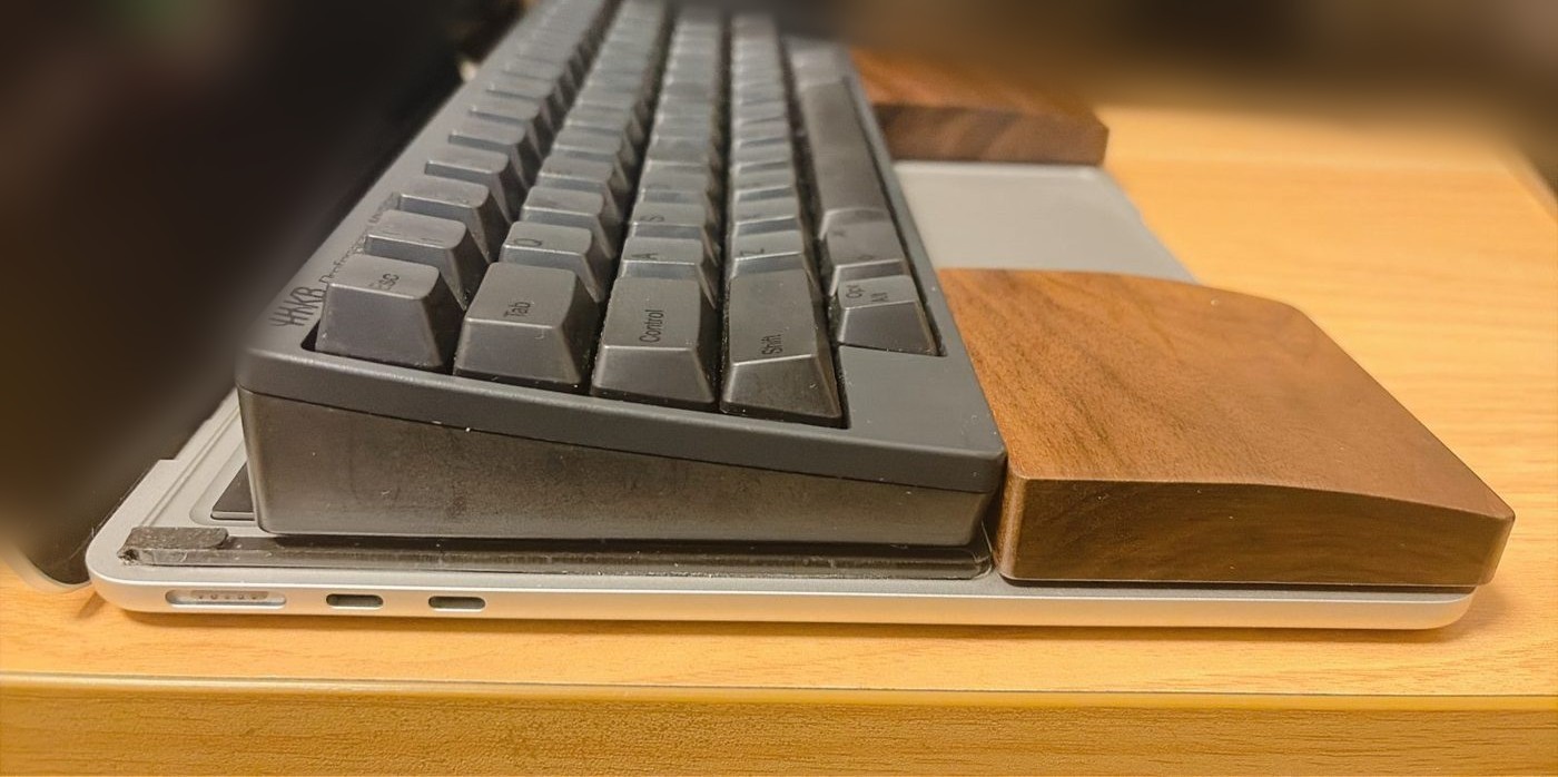 横から見たところ(MacBook の上にアクリル板、その上に HHKB とパームレスト)